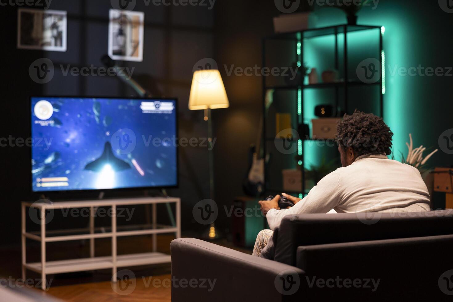 BIPOC man in home theatre using cloud gaming service to play demanding science fiction videogame on smart TV. Gamer enjoying high quality game, streaming it online, flying spaceship with controller photo