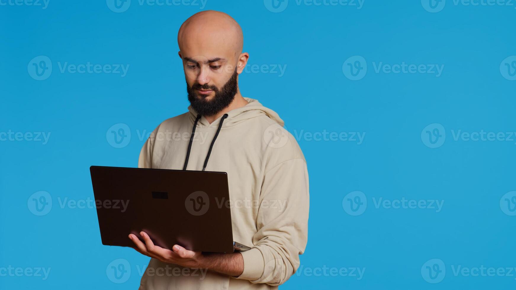 Middle eastern man works with cyber security on laptop, trying to do some software programming and report bugs. Young adult operating as a system developer in studio. Camera 2. Handheld shot. photo
