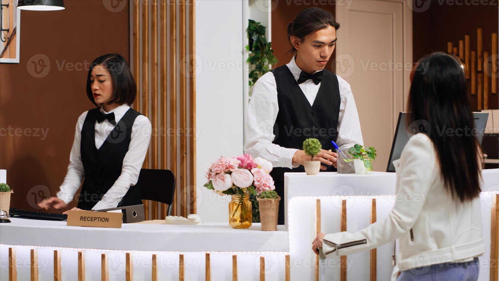 Receptionist examining passport information to do check in for customer, asian woman arriving at front desk after long flight. Employee doing id verification to confirm reservation. Handheld shot. photo