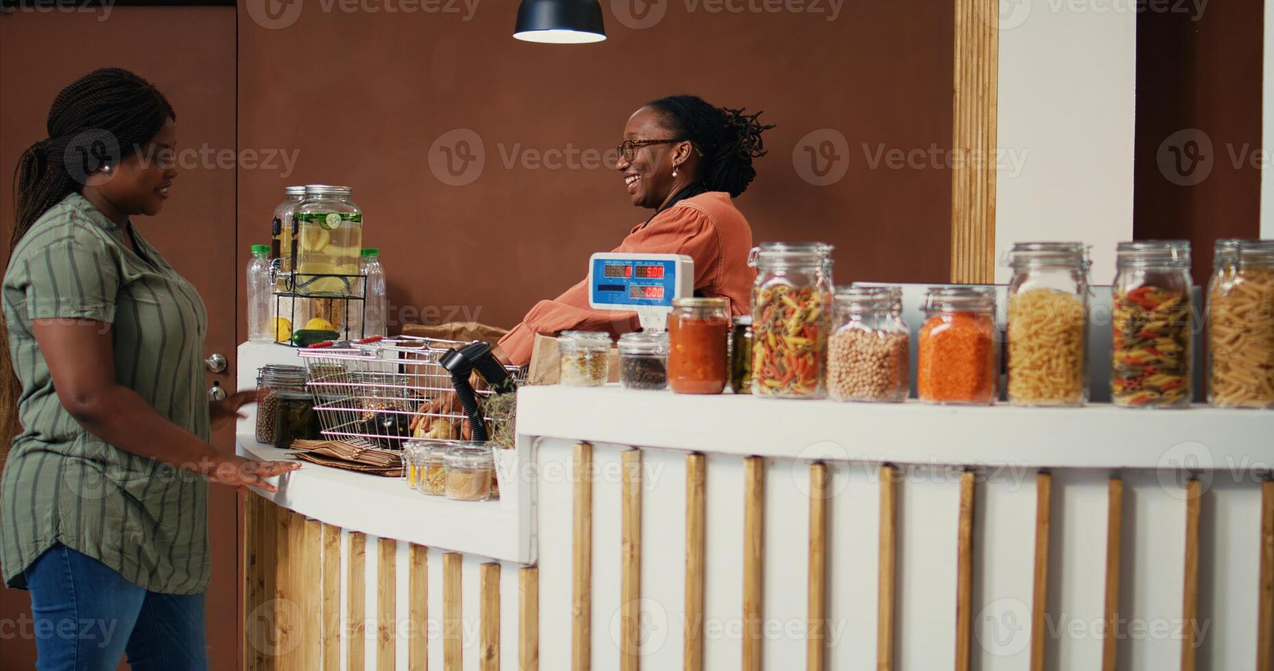 African american woman buying freshly harvested produce from local grocery store, searching for natural ripe fruits and veggies. Merchant weighting goods on scale for customer. Handheld shot. photo