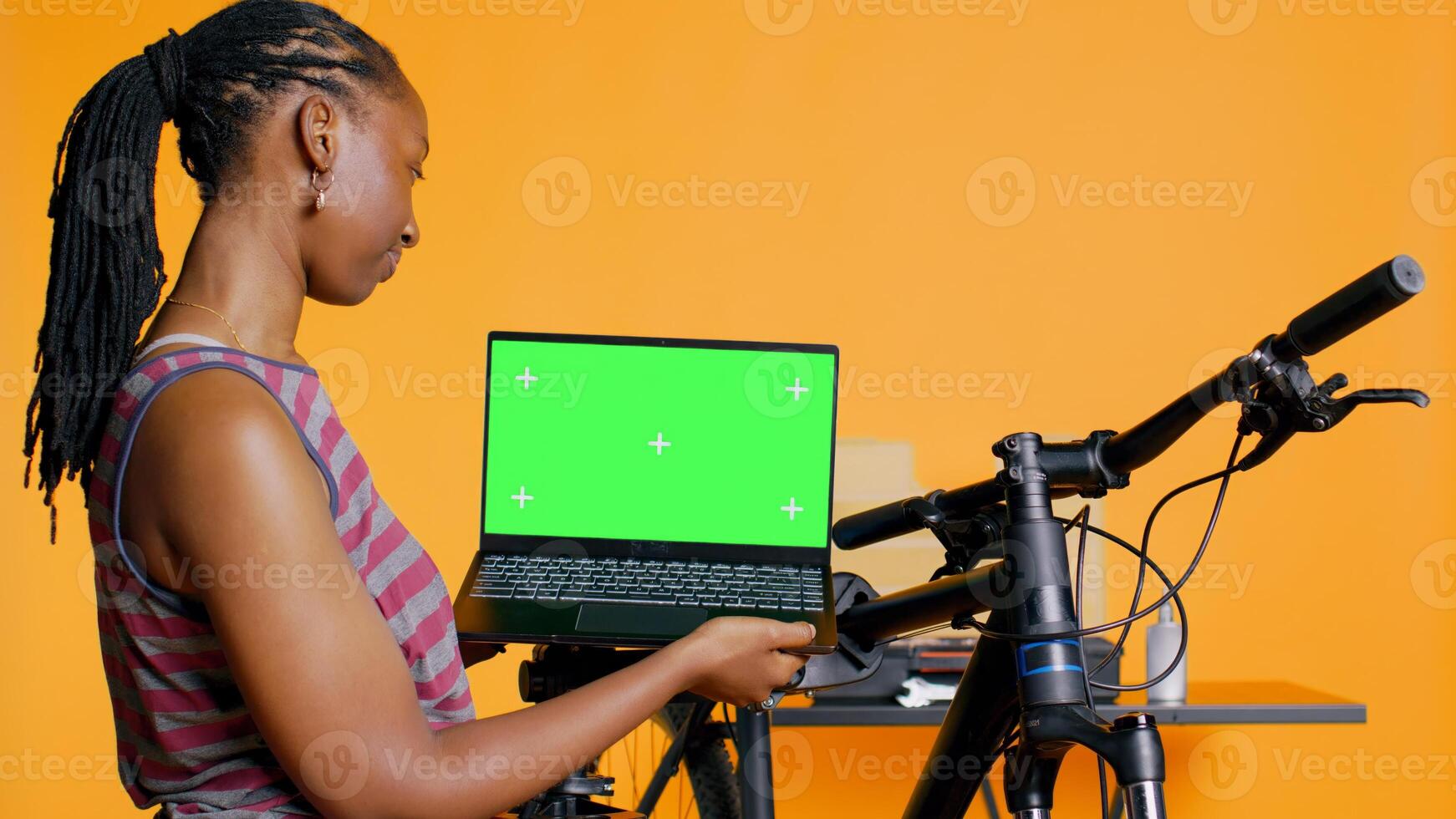 Cheerful woman following tutorial videos on chroma key laptop, learning to fix bike. BIPOC cycling hobbyist having fun repairing bicycle, following online guide on isolated screen notebook photo