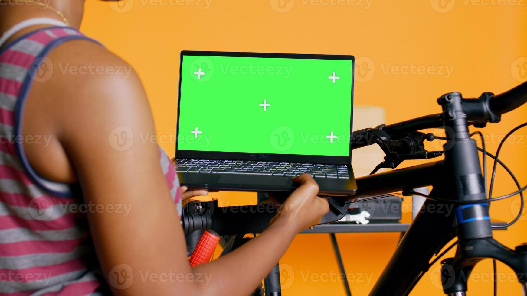 Mechanic doing bike servicing in studio background atelier shop, looking on green screen laptop maintenance list. Specialist checking online for replacement bicycle parts on chroma key notebook photo