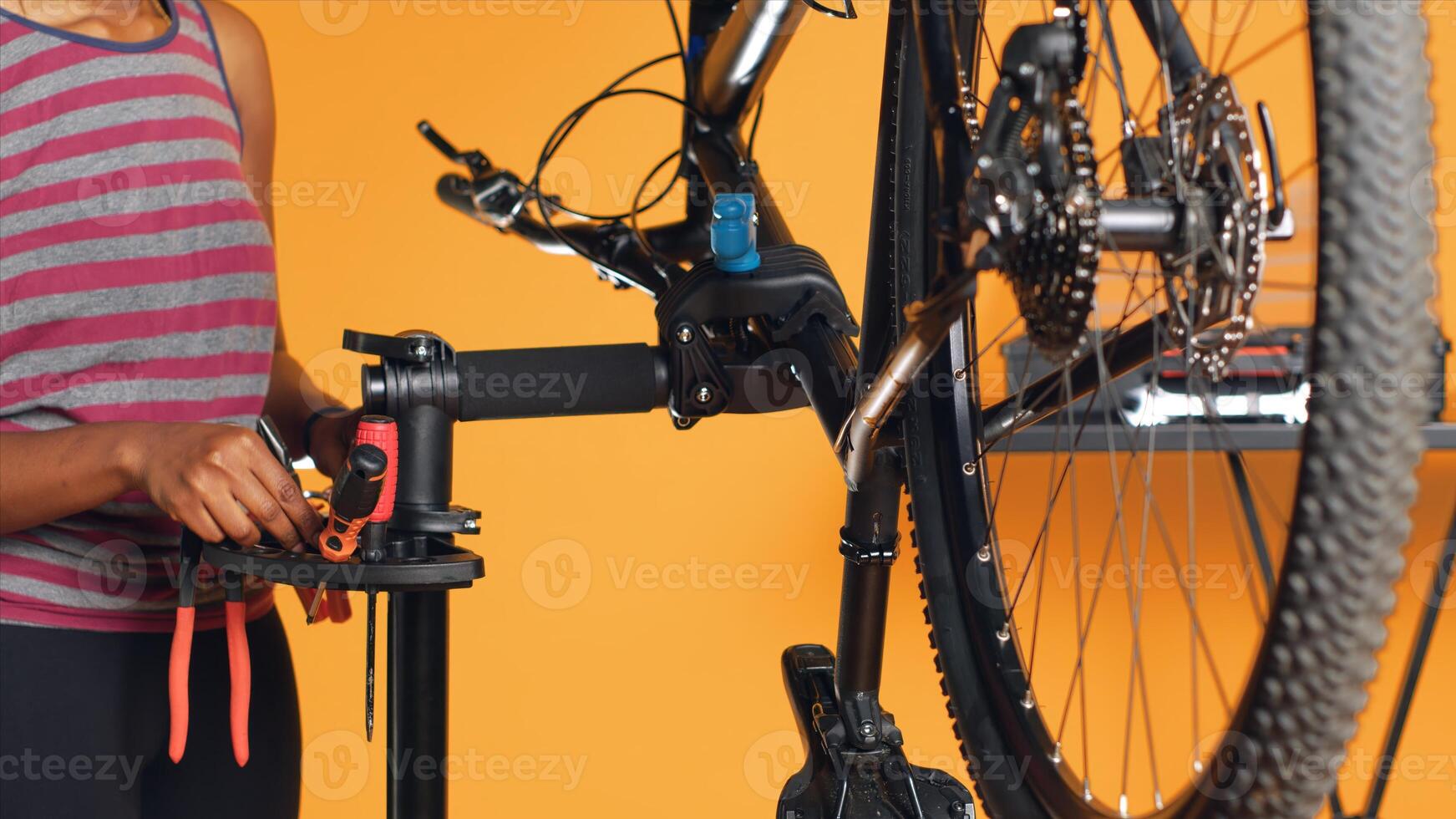African american mechanic utilizing different tools to repair damaged bike handlebar grips, studio background. Employee using specialized gear to fix shifters and brake levers on bicycle, camera A photo