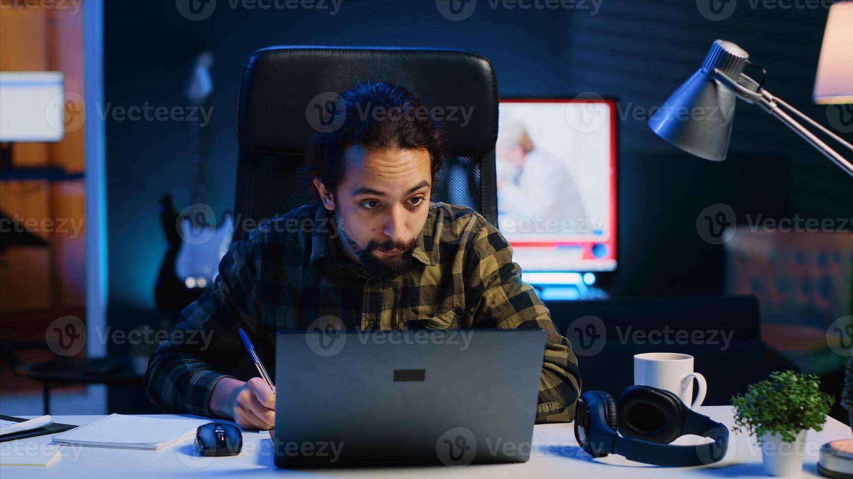 Man at home paying attention in elearning seminar teleconference with teacher, writing memo to remember later. Homeschooling student listening to lesson while taking note of weekend homework photo