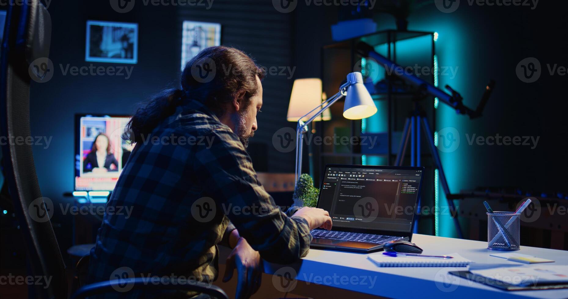 Experienced programmer writes code on laptop screen while in apartment office using Java programming languages. Developer remotely working on fixing database errors while working from home, camera B photo