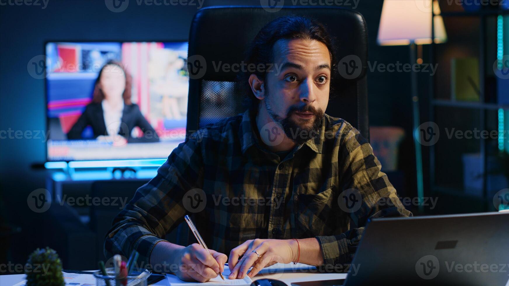 Remote employee working at home office desk, reading information on laptop and writing in notebook. Freelancer noting down ideas on paper using pen while teleworking, camera A photo