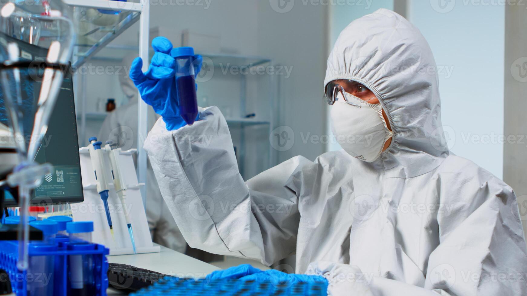 Researcher in coverall testing liquid sample using test tubes for new treatment medical laboratory. Team of doctors examining virus evolution using high tech for vaccine development against covid19 photo