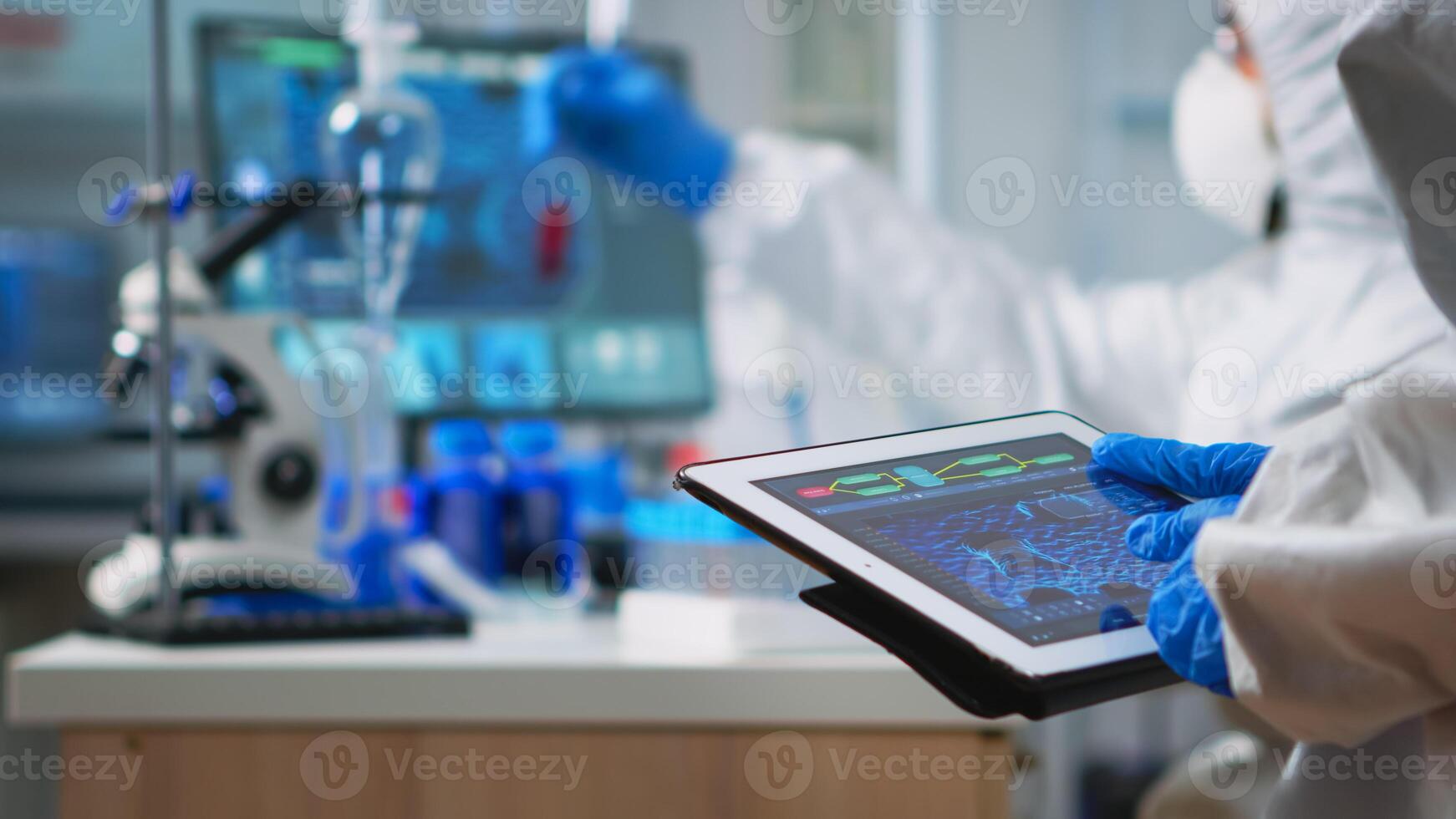 Back view of scientist in coverall analyzing virus evolution looking on digital tablet. Team of microbiologists conducting vaccine development using high tech for researching treatment against covid19 photo