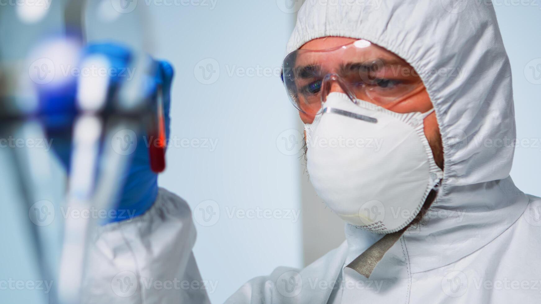 Close up of chemist holding blood sample wearing coverall analysing virus evolution in laboratory. Doctor working with various bacteria, tissue, pharmaceutical research for antibiotics against covid19 photo