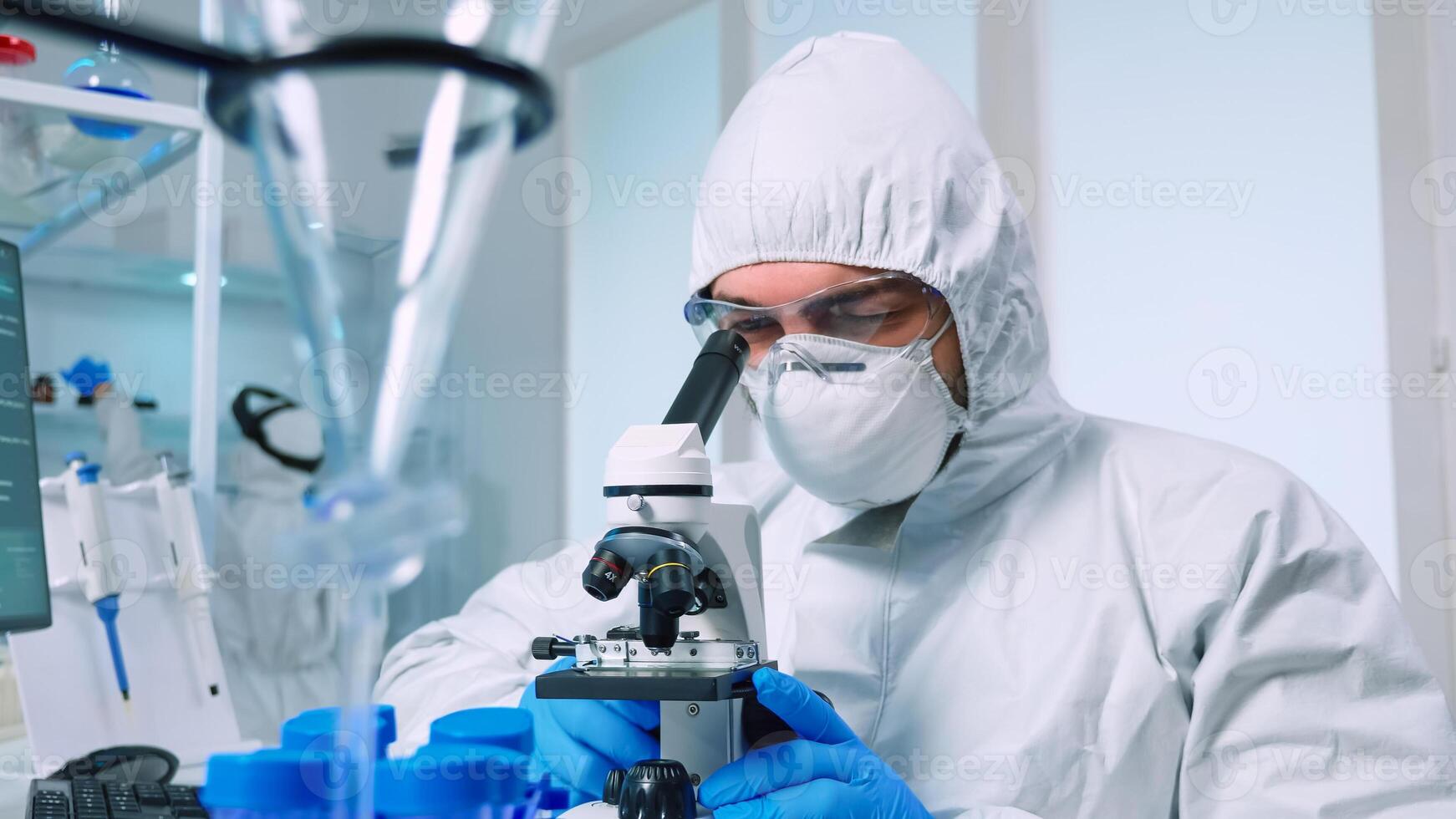 Biotechnology scientist in ppe suit researching DNA in laboratory using microscope. team examining virus evolution using high tech for scientific research of vaccine development against covid19 photo
