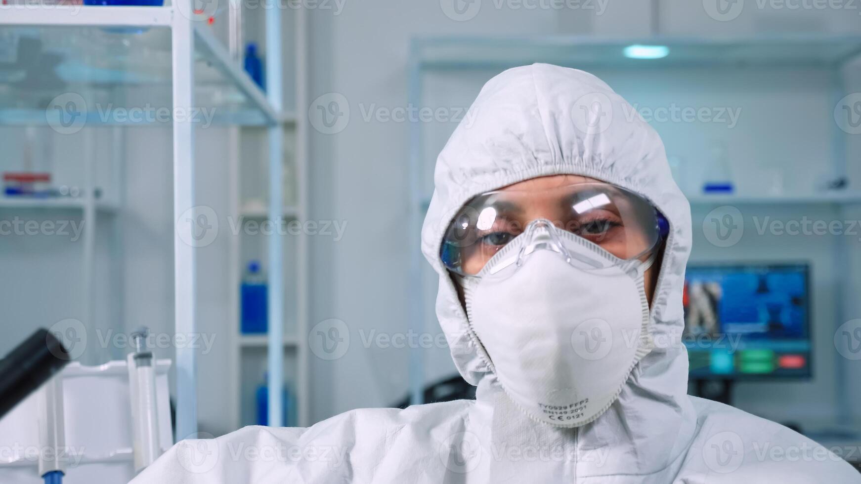 Tired doctor wearing coverall looking exhausted at camera in modern equipped lab. Scientist examining virus evolution using high tech and chemistry tools for scientific research, vaccine development. photo