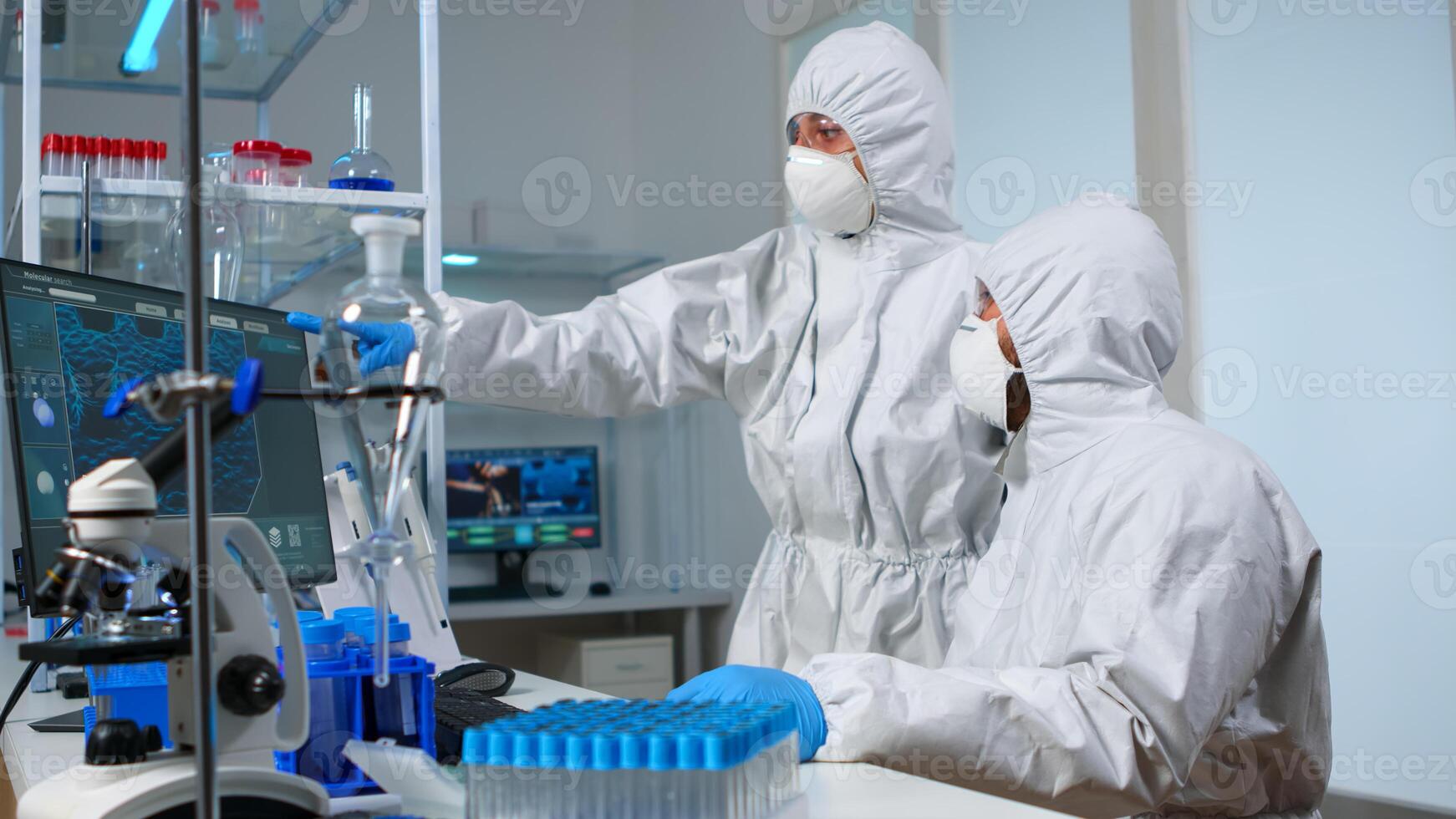 Scientist team in prorection suit arguing in front of pc looking at virus development in equipped laboratory.Team of scientists analysing vaccine evolution using high tech for researching treatment photo