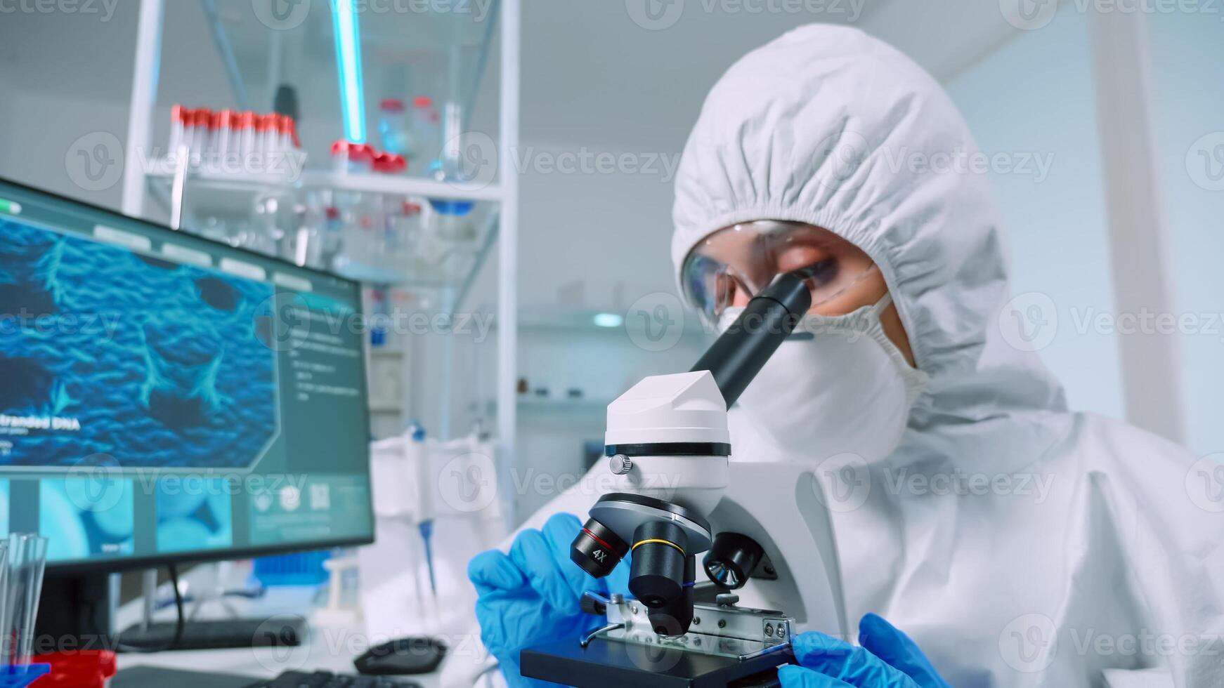Chemist researcher wearing coverall in sterile lab doing experiments for medical industry using microscope. Doctors examining virus evolution using high tech for vaccine development against covid19 photo