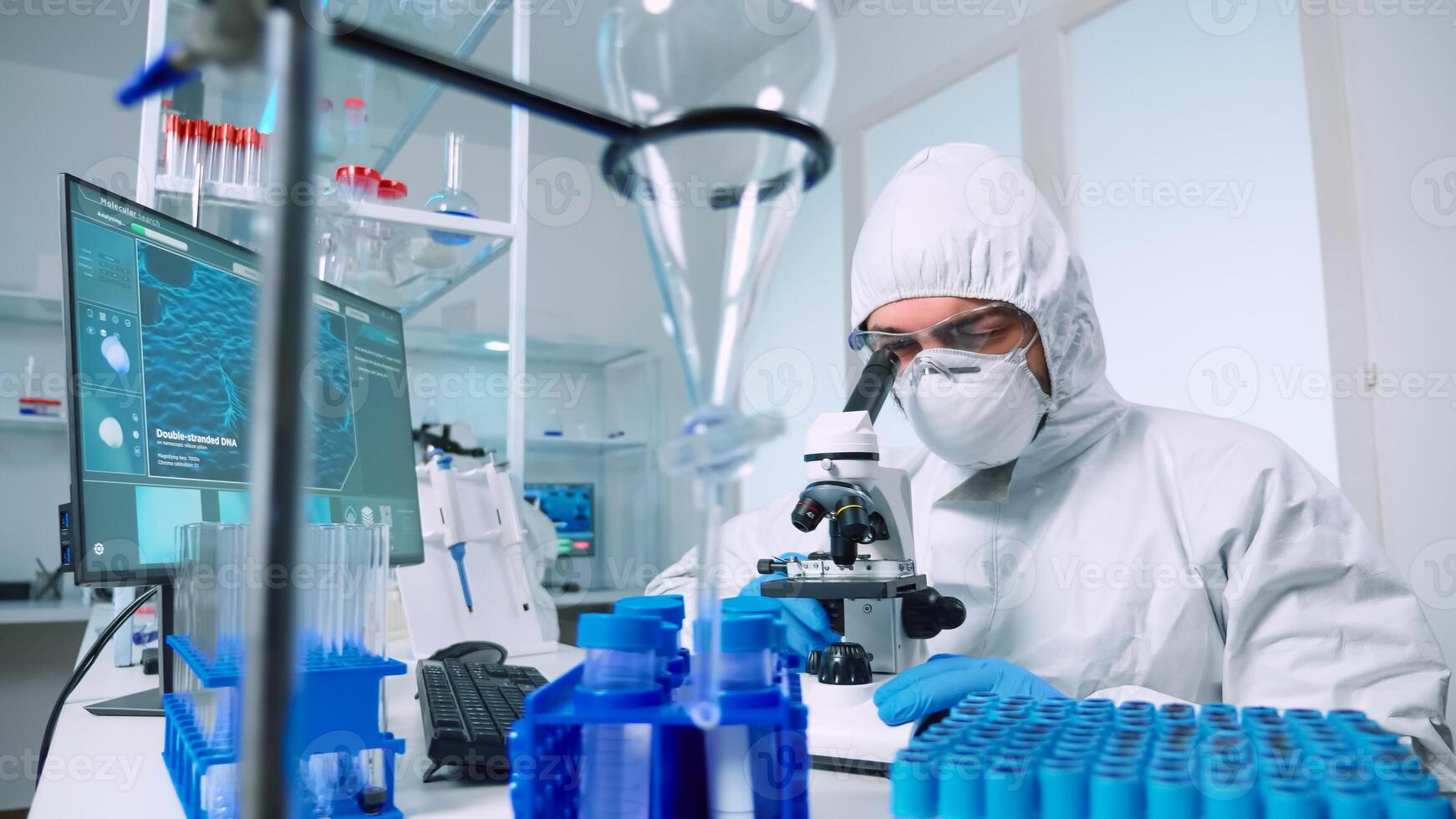 Laboratory scientist in ppe suit conducting experiment looking through a microscope in modern lab. Man working with various bacteria tissue, blood samples, concept of medical research for antibiotics photo