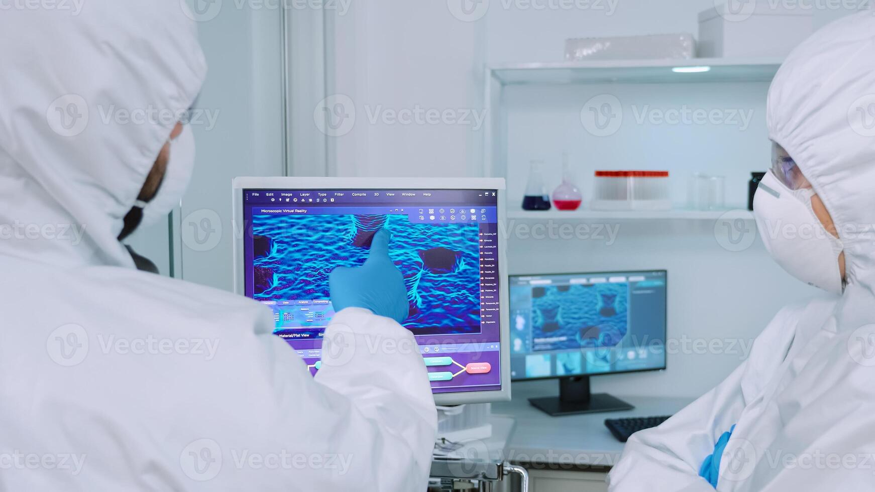 Scientists coworkers in coverall discussing about virus evolution in equipped laboratory pointing on computer desktop. Doctors examining vaccine evolution using high tech researching diagnosis photo