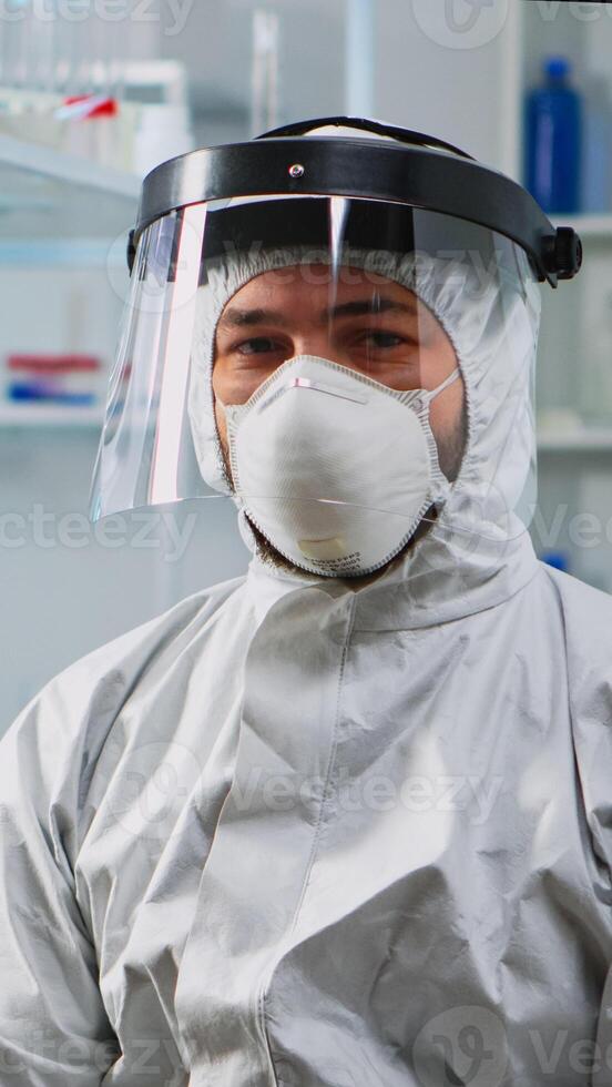 Tired doctor in protection suit against covid-19 looking exhausted at camera in equipped lab. Team of scientists examining virus evolution using high tech for scientific research, vaccine development. photo