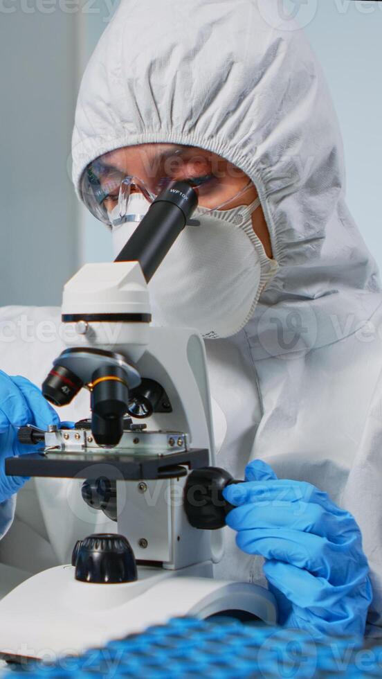 Woman research scientist wearing ppe suit looking at samples under microscope in equipped laboratory. Doctor working with various bacteria, tissue, blood tests, pharmaceutical research for antibiotics photo