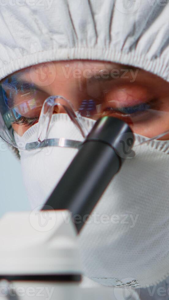 Close up of experienced biologist in ppe suit working on microscopes in equipped laboratory. Chemist in coverall examining vaccine evolution using high tech researching diagnosis against covid19 virus photo