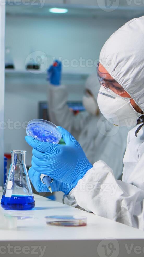 Chemist in ppe suit using micropipette for filling test tubes in modern equipped laboratory. Team of scientists examining virus evolution using high tech for vaccine development against covid19 photo