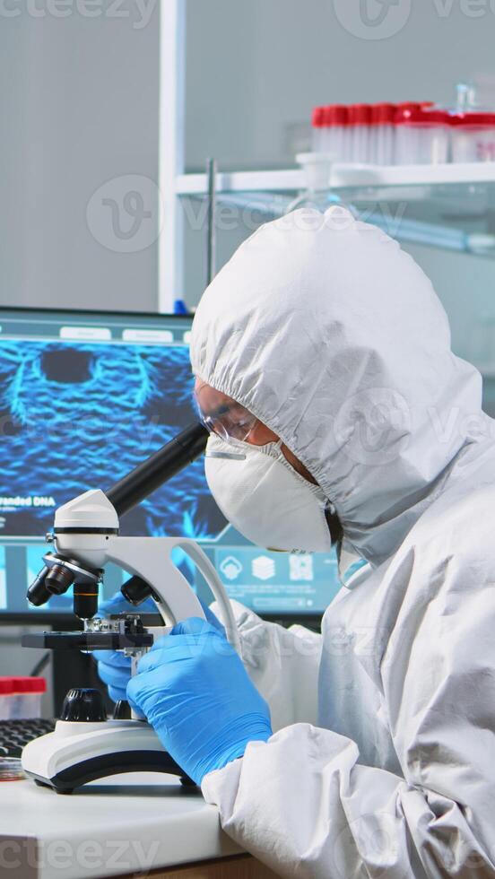 Chemist researcher in overall looking at bacteria sample from glass equipment in modern equipped laboratory. Examining vaccine evolution using high tech for researching treatment against covid19 virus photo