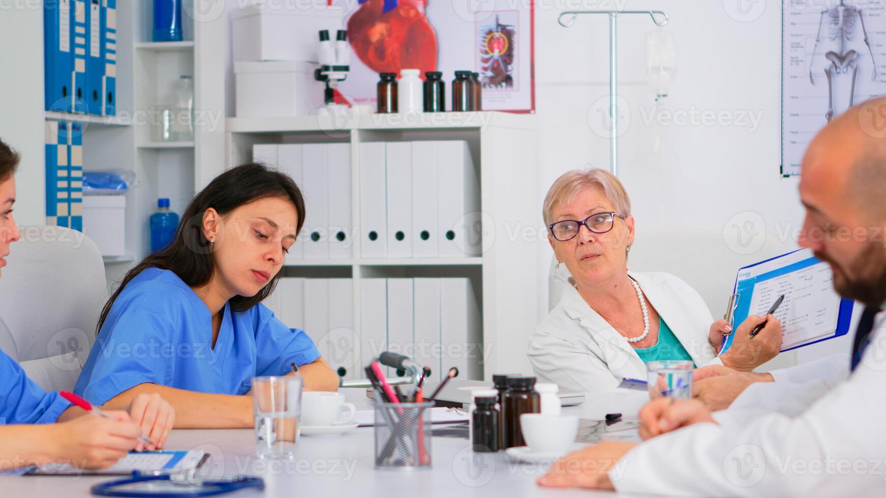 Senior specialist doctor is brainstorming to analyze medical problems pointing on clipboard showing medical statistics. Team of doctors working in hospital office discussing symptoms of disease photo