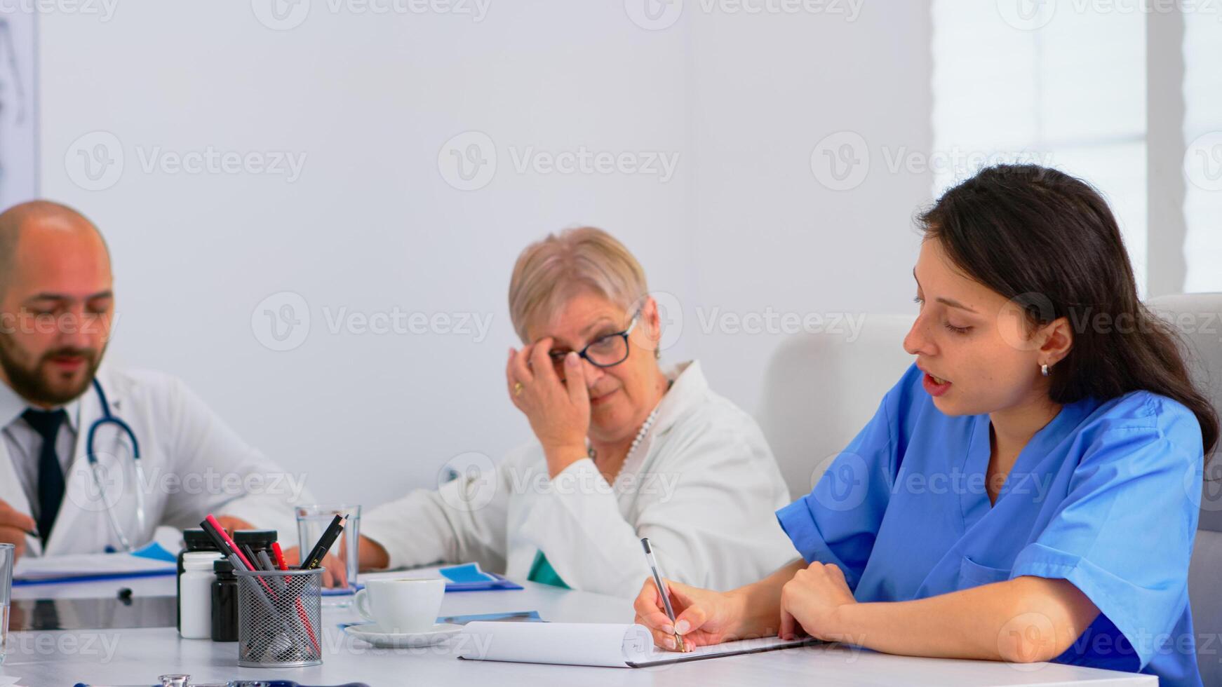 Team of doctors having medical conference dividing their tasks, discussing about patients problems sitting at desk in hospital meeting office. Group of physicians talking about symptoms of disease photo