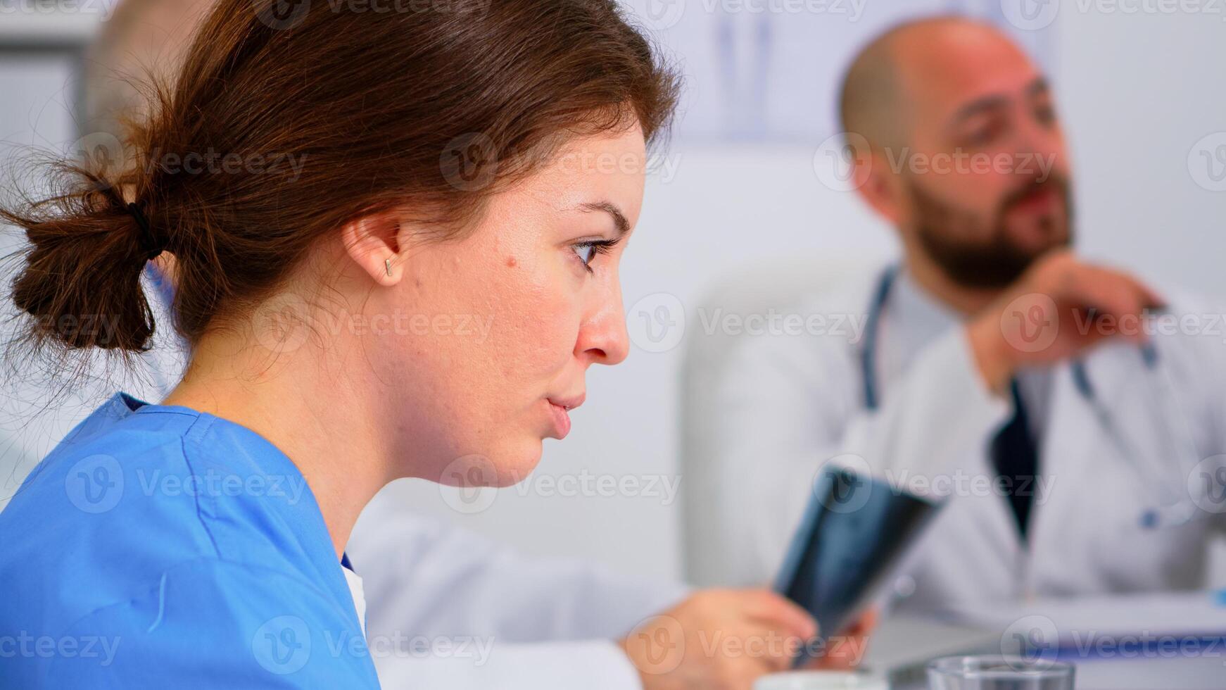 Close up of young woman nurse discussing with colleague during medical conference sitting on desk in hospital meeting office. Talking about symptoms of disease in clinic room during brainstorming photo