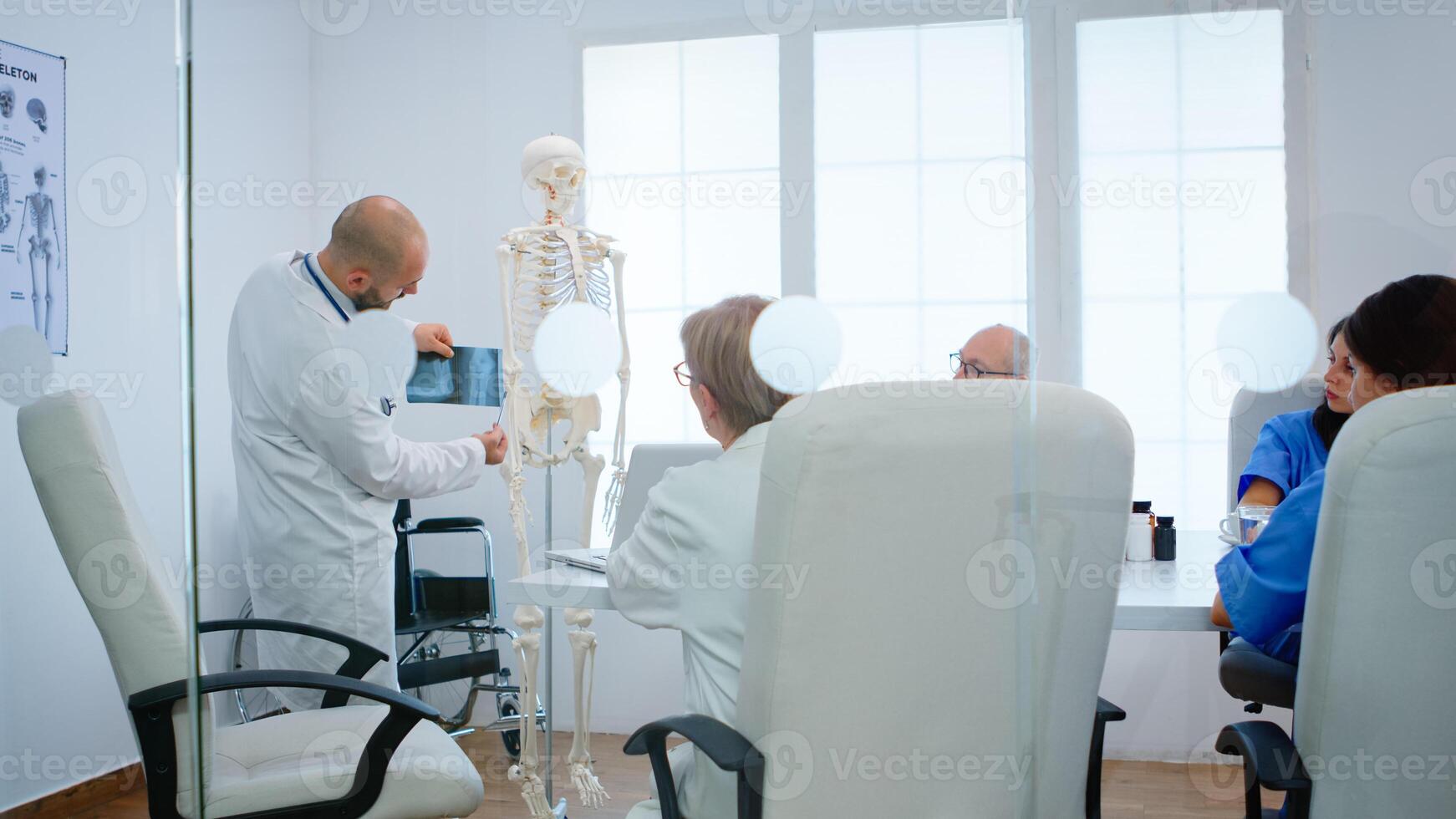 Professional physician learning colleagues body bone functionson using radiography and human skeleton anatomical model standing in hospital office. Physicians discussing about symptoms of disease photo