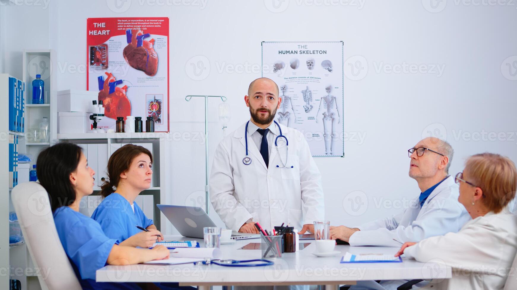 Young specialist doctor explaining diagnosis for patients treatment issues record using virtual reality in workplace. Discussing with medical team during brainstorming, coworkers taking notes. photo