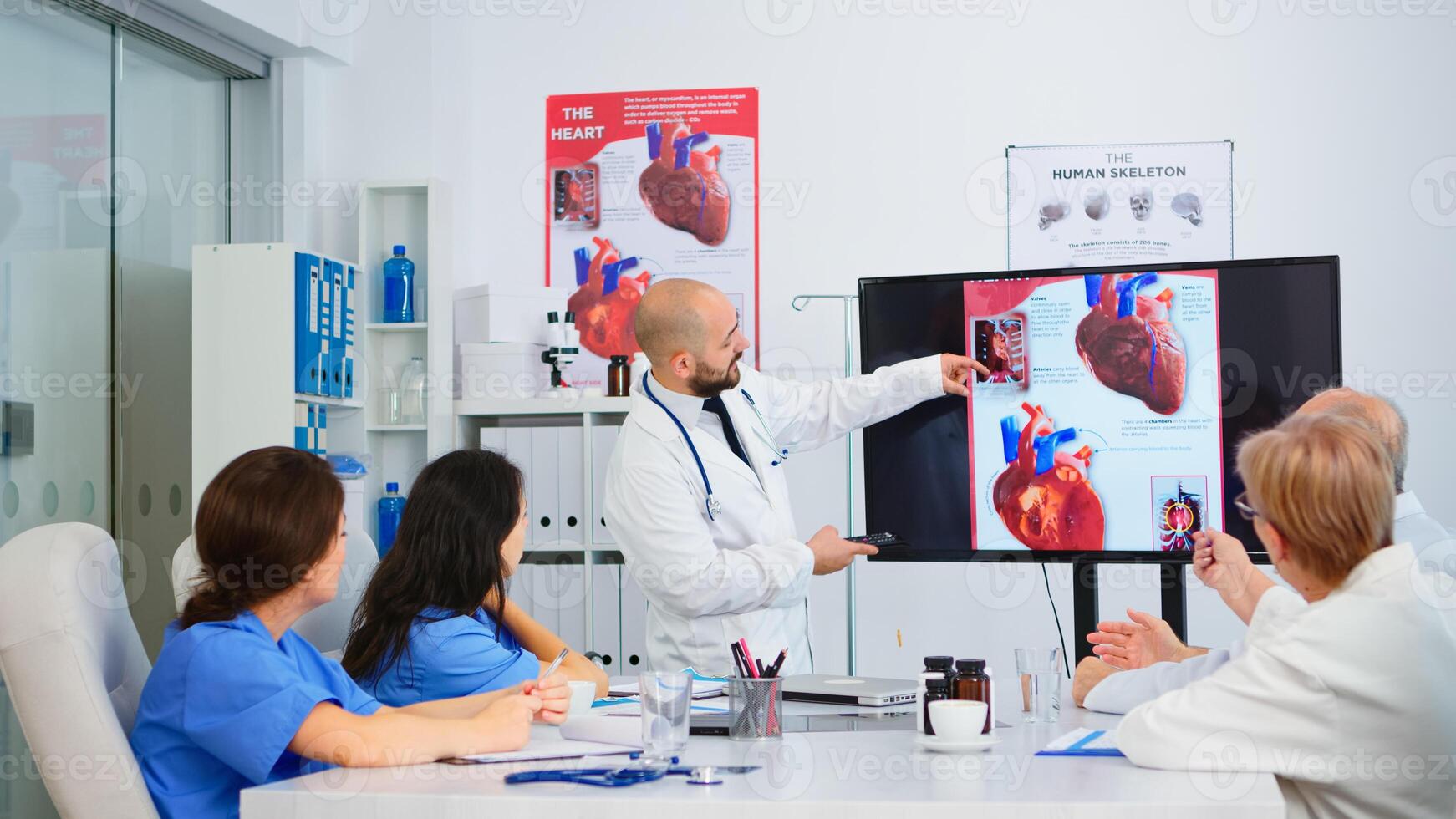 Experienced man doctor analysing heart issues image together with cvalified colleagues in meeting room, pointing on monitor. Doctors discussing diagnosis about treatment of patients photo