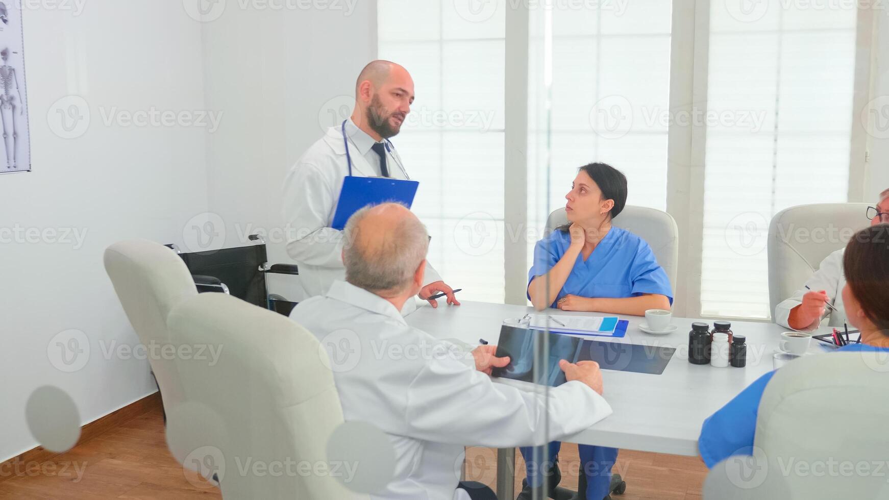 Medical practitioner presenting diagnosis to colleagues holding clipboard during briefing with coworkers. Clinic expert therapist talking with colleagues about disease, medicine professional photo