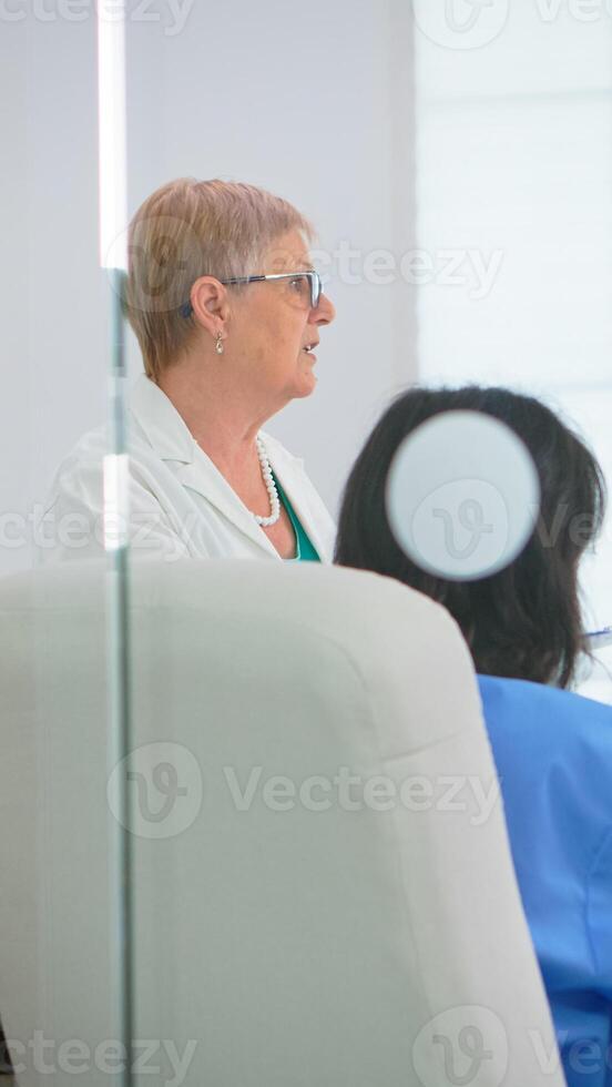 Medical team sitting and discussing at table in hospital meeting office using tablet and clipboard with documents of patients. Group of physicians talking about symptoms of disease in clinic office photo