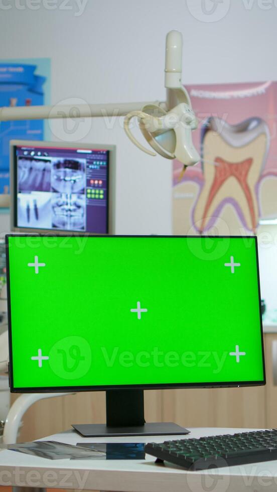 Computer with green screen placed in front of camera in empty modern equipped stomatological room. Stomatology clinic with nobody in it prepared for next patient with mock-up, chroma key pc display photo