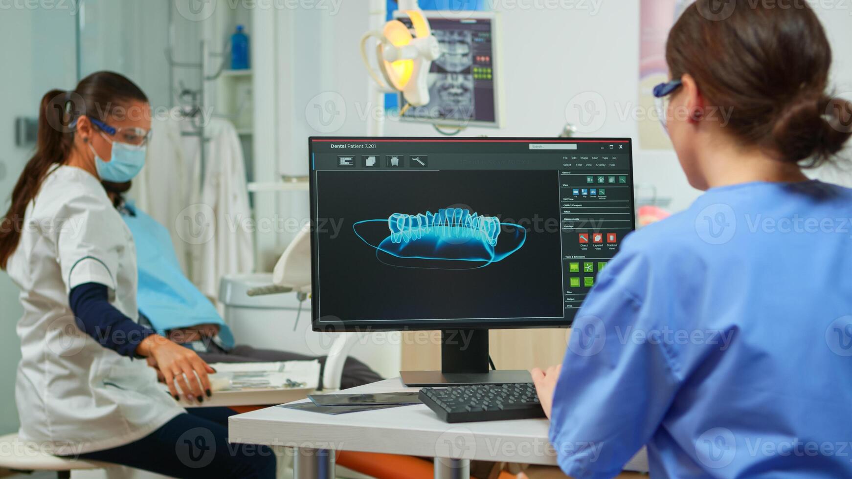 Dentist assistant writing parameters from digital dental fingerprint of patient, while specialist doctor with face mask speaks to man with toothache sitting on stomatological chair preparing tools photo