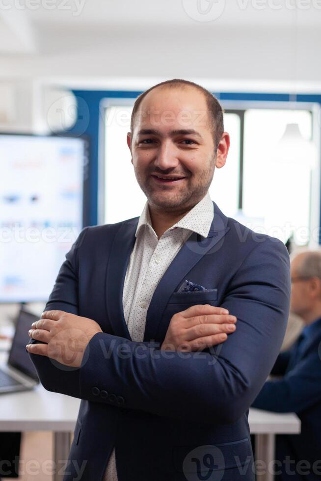Young man entrepreneur smiling in front of camera standing in brainstorming room, preparing for meeting with partners. Manager working in professional start up financial business, modern company workplace ready for meeting. photo