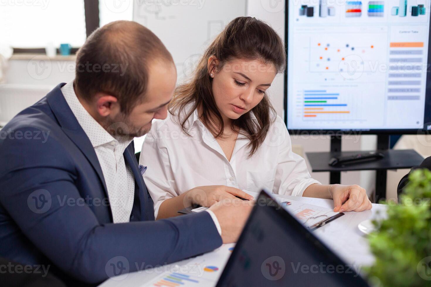 Colleagues of startup business discussing looking at documents in company board brainstorming conference room checking graphs and charts. Financial analysis during briefing. photo