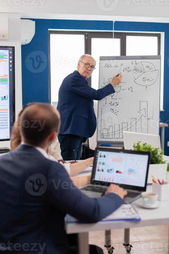 Confident man business coach giving flipchart presentation training diverse workers group at workshop, Serious speaker boss executive, business trainer explaining development strategy to motivated mixed race employees. photo