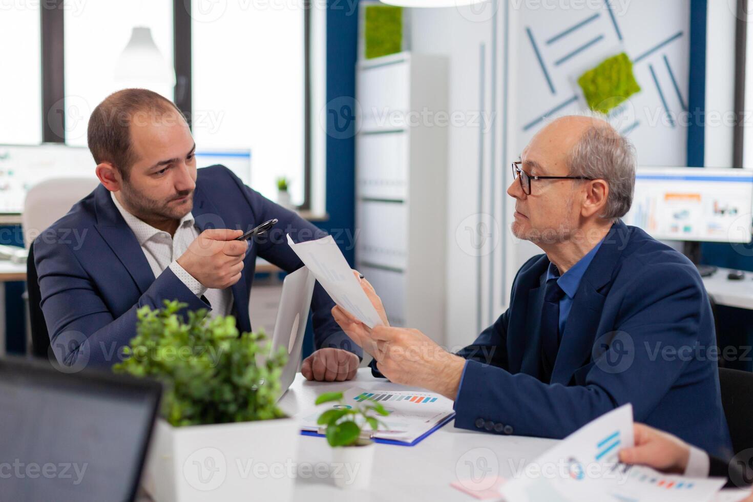 Senior entrepreneur discussing with coworker holding documents in conference during briefing Businessman discussing ideas with colleagues about financial strategy for new start up company. photo