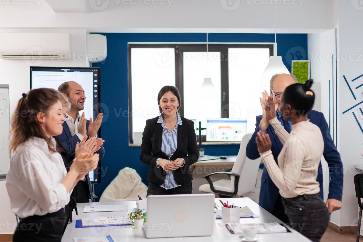 Happy overjoyed financial startup team standing clapping a in conference briefing. Multiethnical partners coworkers celebrate successful teamwork result at company briefing photo