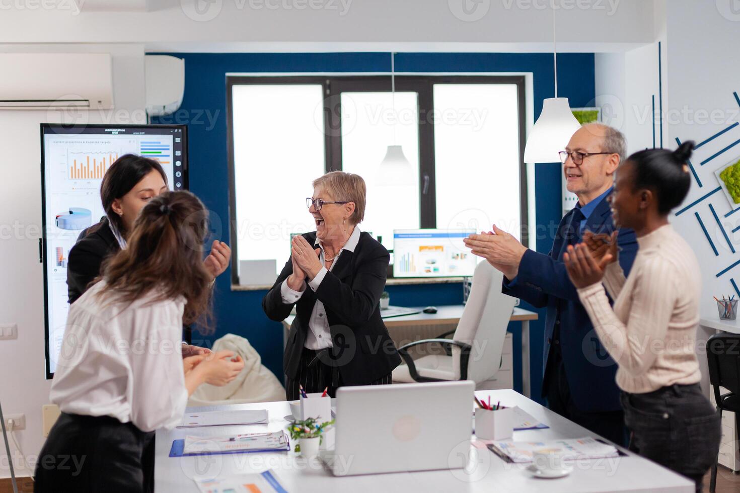 Victorious overjoyed diverse team of businesspeople clapping together in conference room. Multiethnical partners coworkers celebrate successful teamwork result at company briefing photo