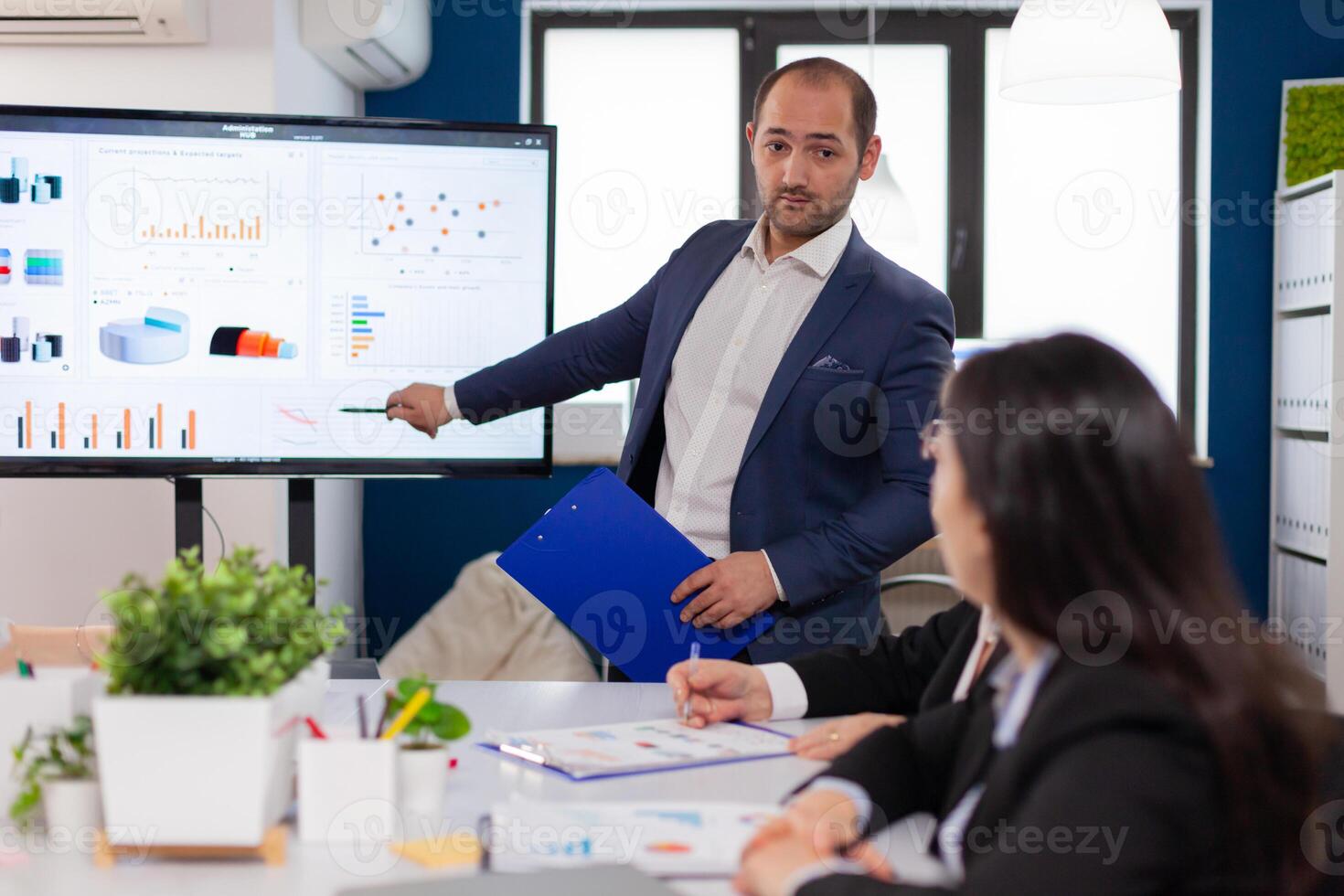 Successful team leader briefing pointing explaining project in conference room brainstorming. Corporate staff discussing new business application with colleagues looking at screen photo