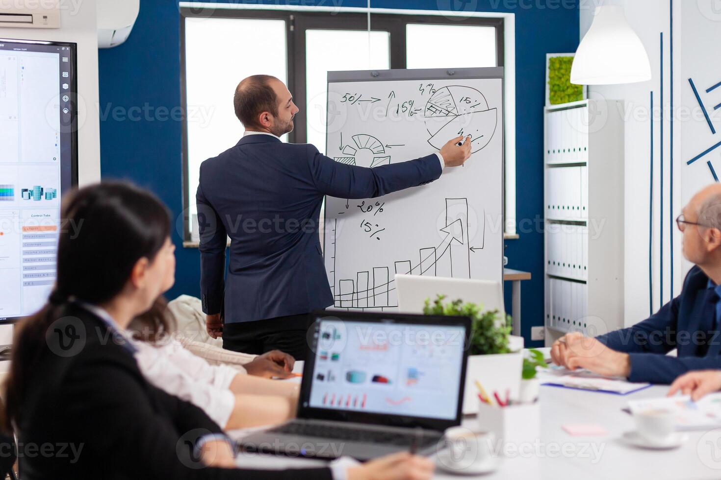 Professional business coache company leader teacher offering flip chart presentation explaining graphs. Serious speaker boss executive, business trainer explaining development strategy to motivated mixed race employees. photo