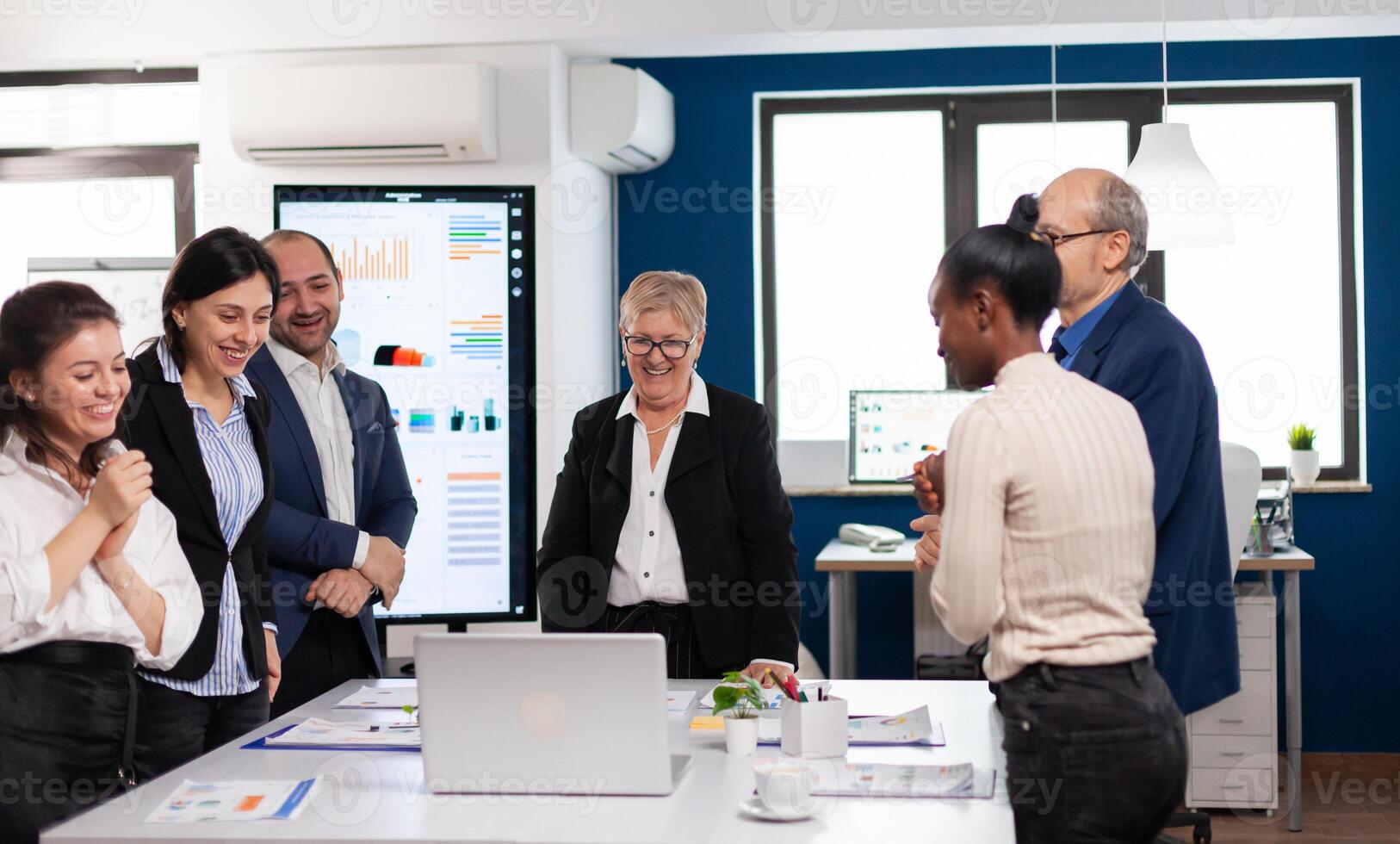 Financial corporate team overjoyed in conference room looking at laptop. Multiethnical partners coworkers celebrate successful teamwork result at company briefing photo