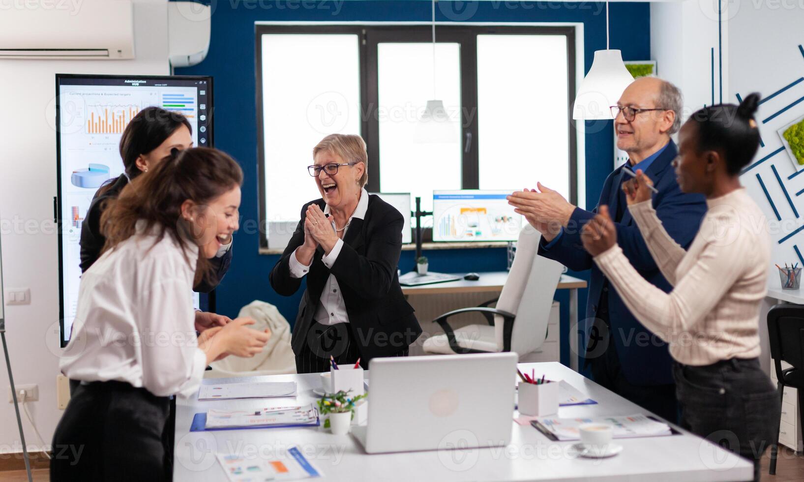 Victorious overjoyed diverse team of businesspeople clapping together in conference room. Multiethnical partners coworkers celebrate successful teamwork result at company briefing photo