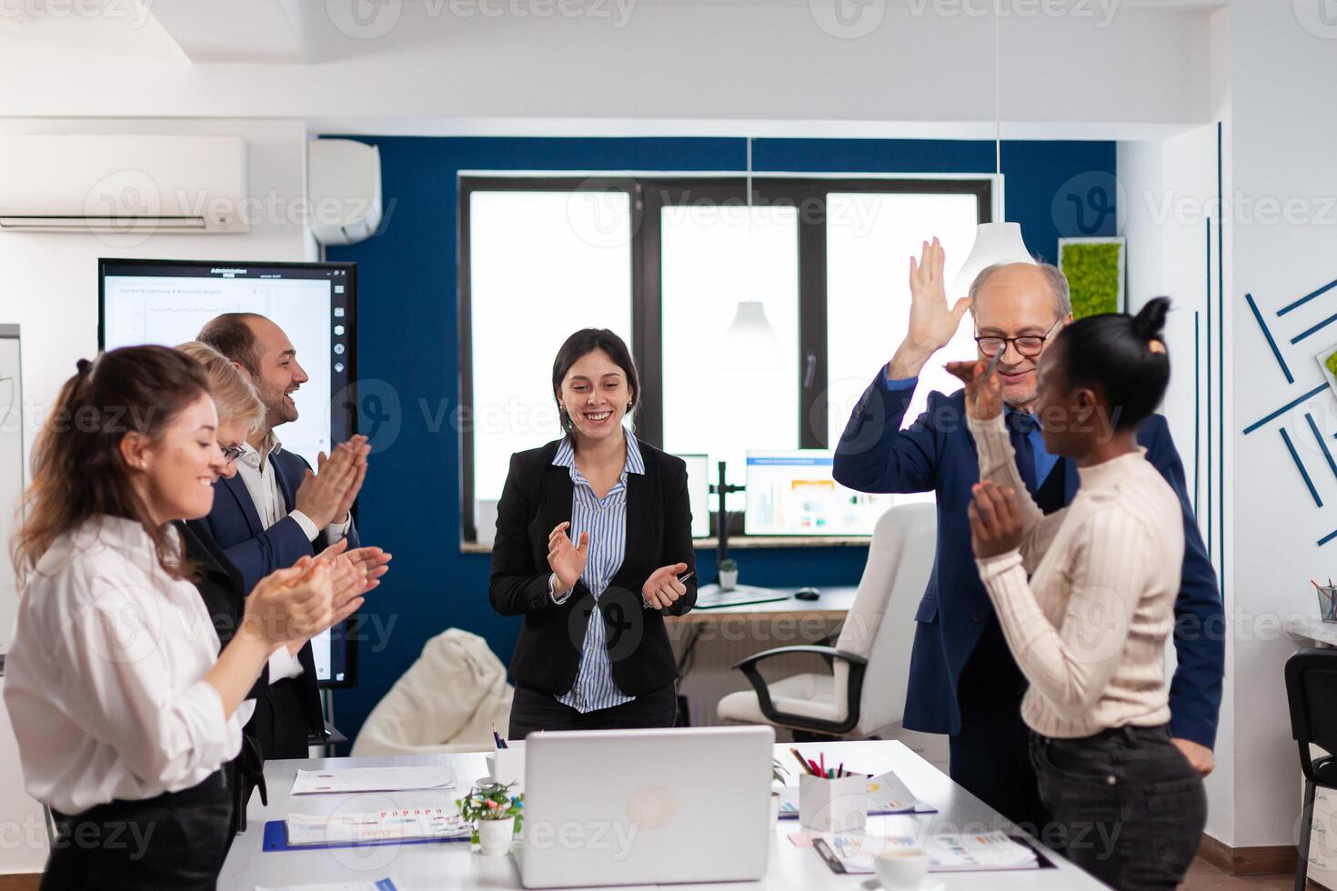 Happy overjoyed financial startup team standing clapping a in conference briefing. Multiethnical partners coworkers celebrate successful teamwork result at company briefing photo