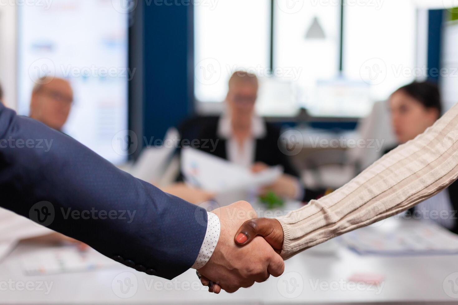 Close up of multiracial business partners standing in front of conference desk shaking hands after signing partnership contract. Diverse team being happy for successful negotiations in startup company photo