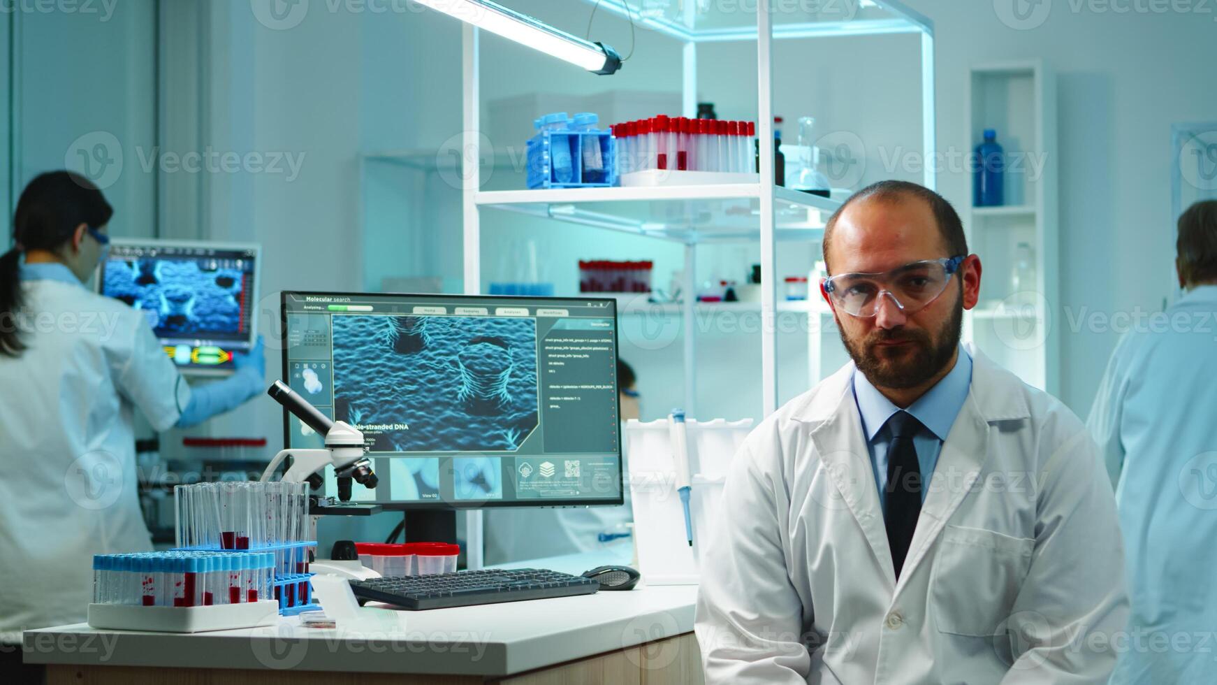 Portrait of exhausted chemist looking at camera in modern equipped lab late at night. Team of biochemists examining virus evolution using high tech and chemistry tool for research, vaccine development photo