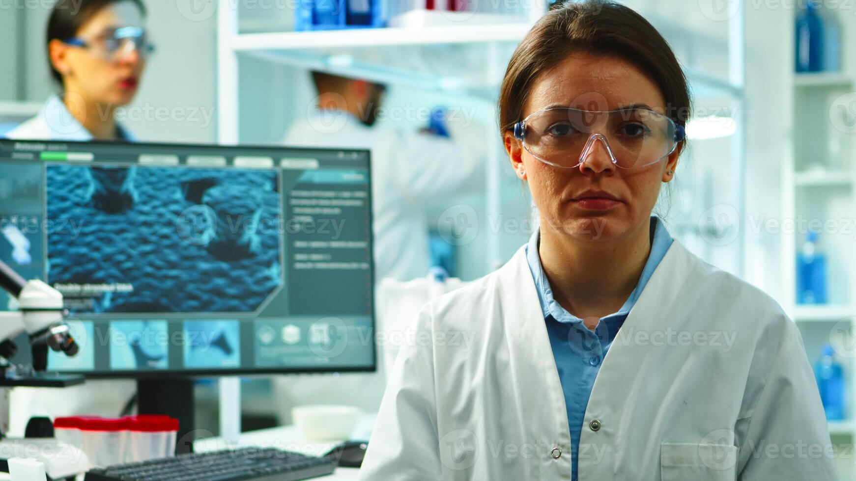 Close up of scientist nurse looking tired at camera sitting in modern equipped laboratory late at night. Team of specialists examining virus evolution using high tech for research, vaccine development photo