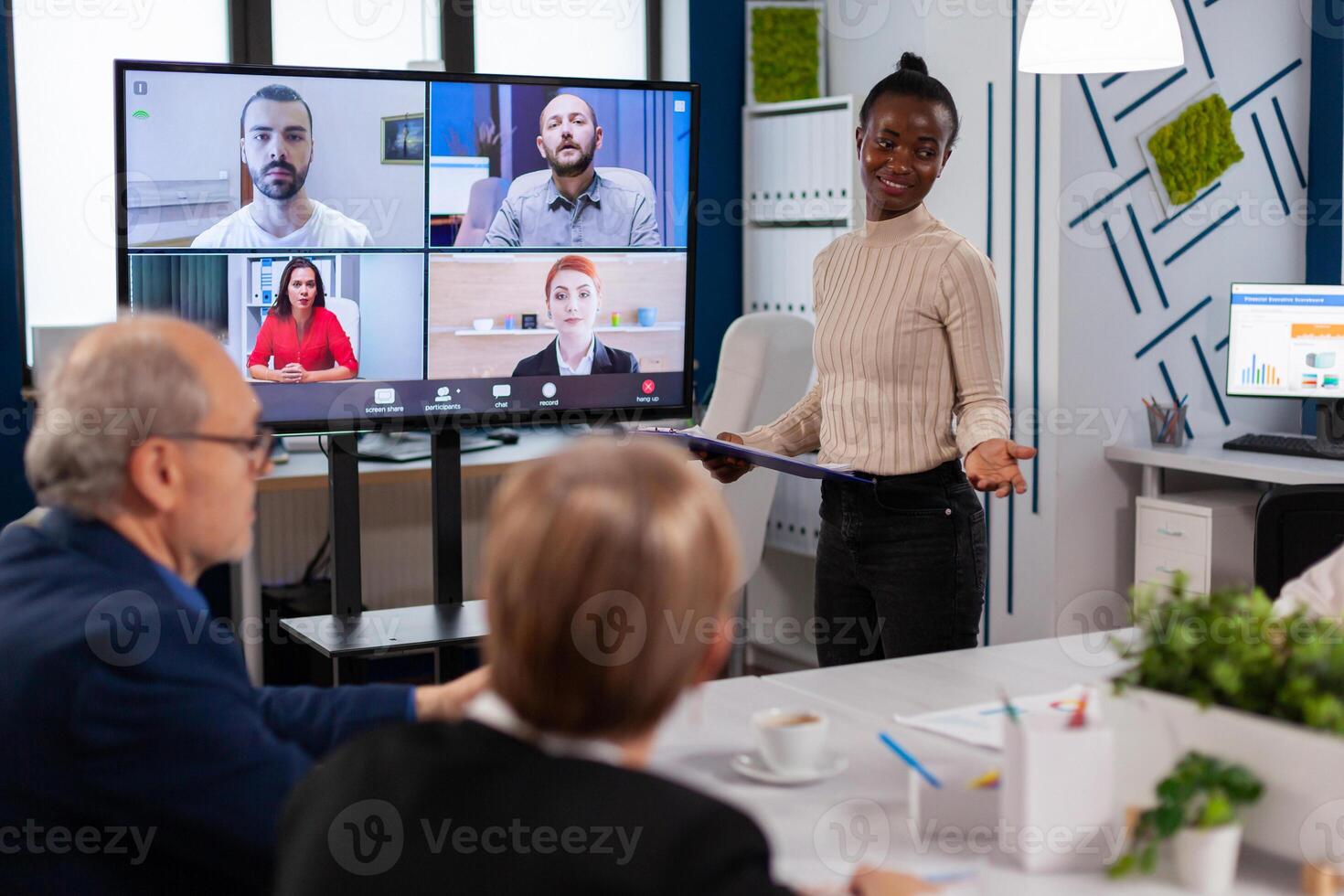 Black manager woman talking with remotely colleagues on call at tv screen, presenting new business partners. Business people talking to webcam, do online conference participate internet brainstorming, distance office discussion. photo