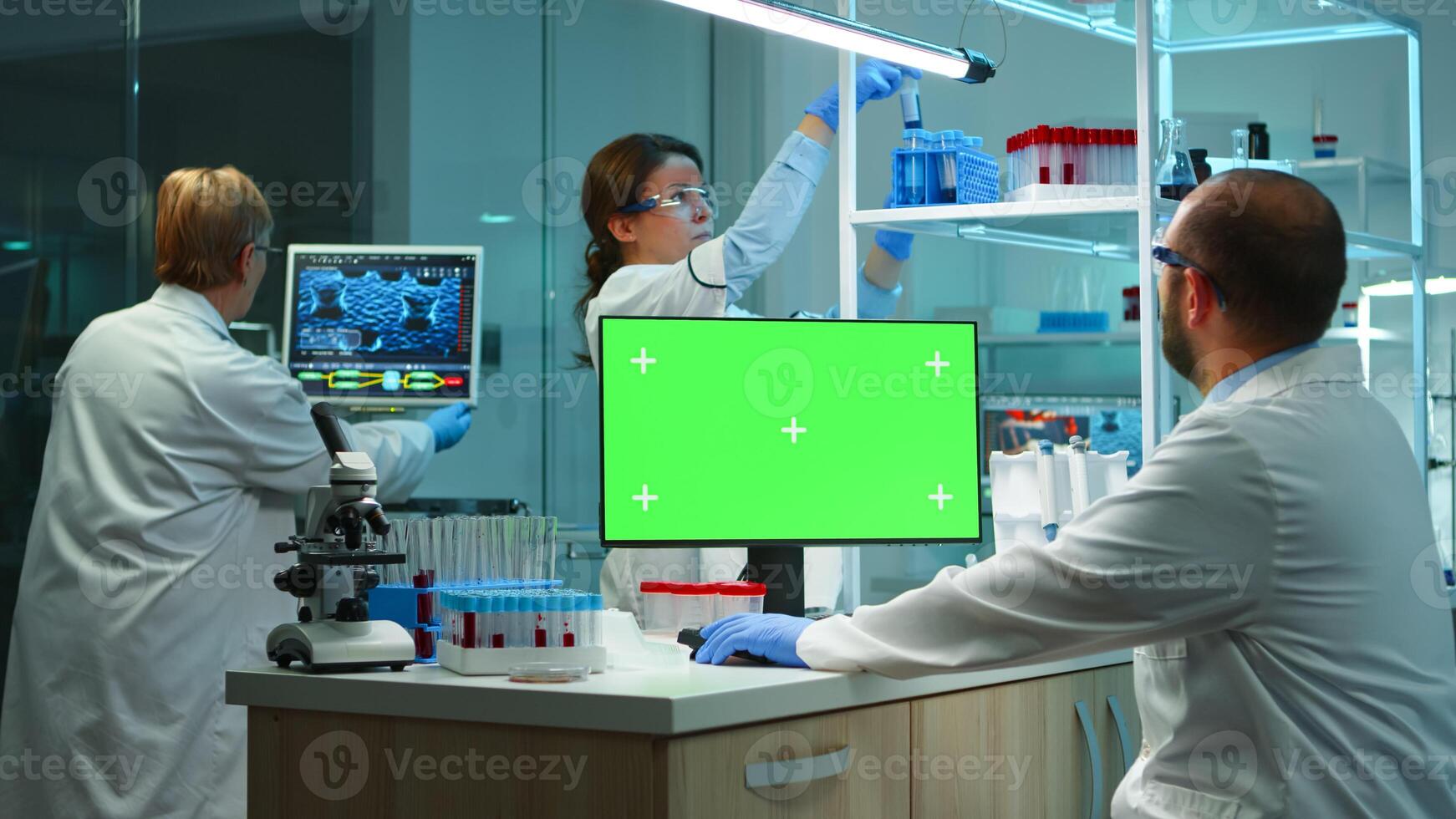 Scientist man typing on computer with green mockup in modern equipped lab working late at night. Team of microbiologists doing vaccine research writing on device with chroma key, isolated display. photo